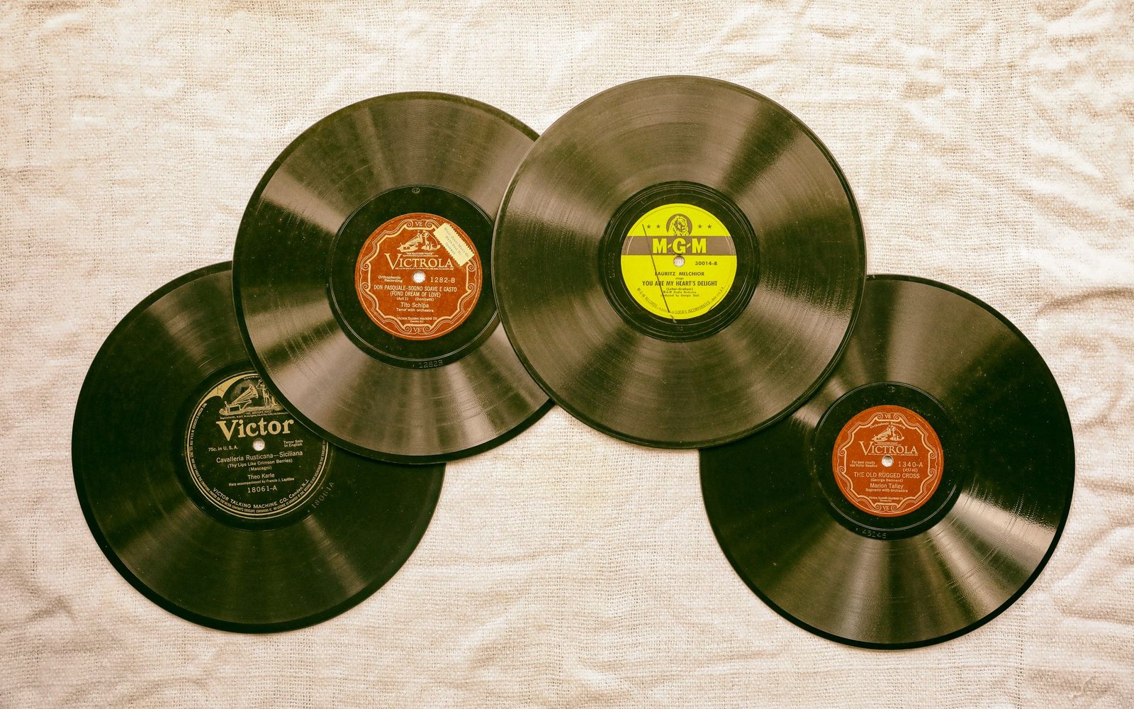 Four vintage 78 RPM shellac records with Victor, Victrola and MGM labels overlapping on fabric